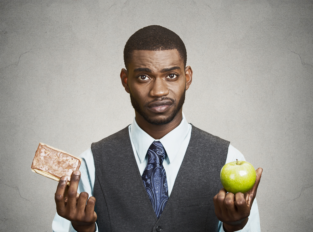 Closeup portrait headshot corporate executive, businessman trying to decide on diet, sweet cookie versus green fresh apple isolated black grey background. Weight control eating habits. Face expression
